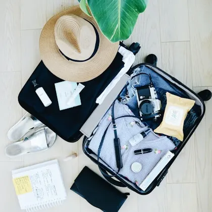 An open suitcase packed for a trip, with a straw hat and travel essentials laid out beside it