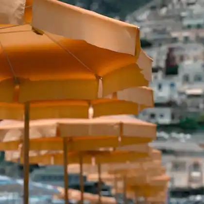 Rows of orange sun umbrellas on a beach, with a colorful coastal town in the background