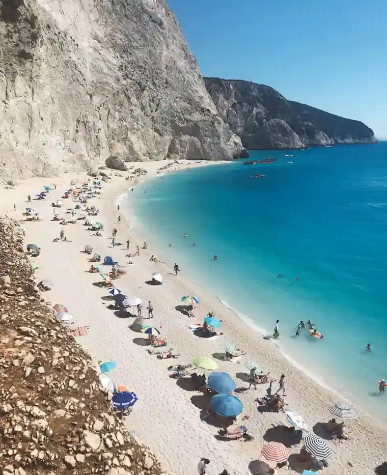 Sunbathers and swimmers along a turquoise beach beneath pale cliffs