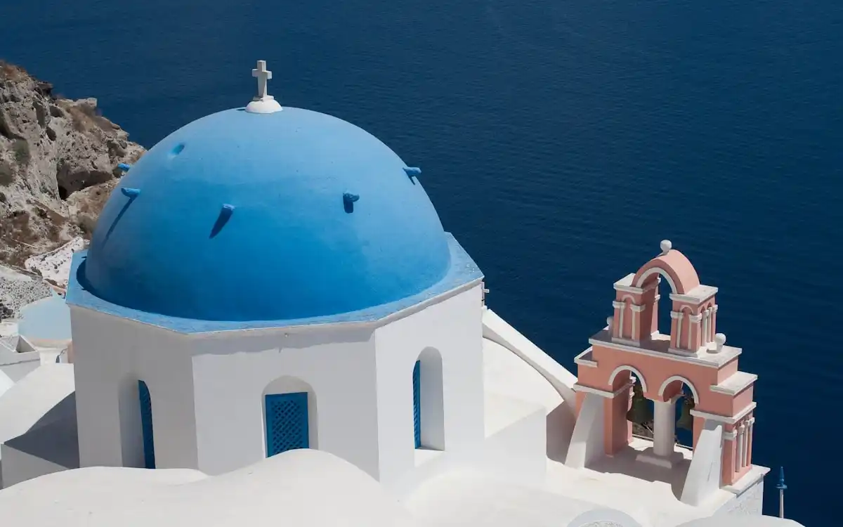A blue-domed church overlooking the deep blue Aegean Sea in Santorini, Greece