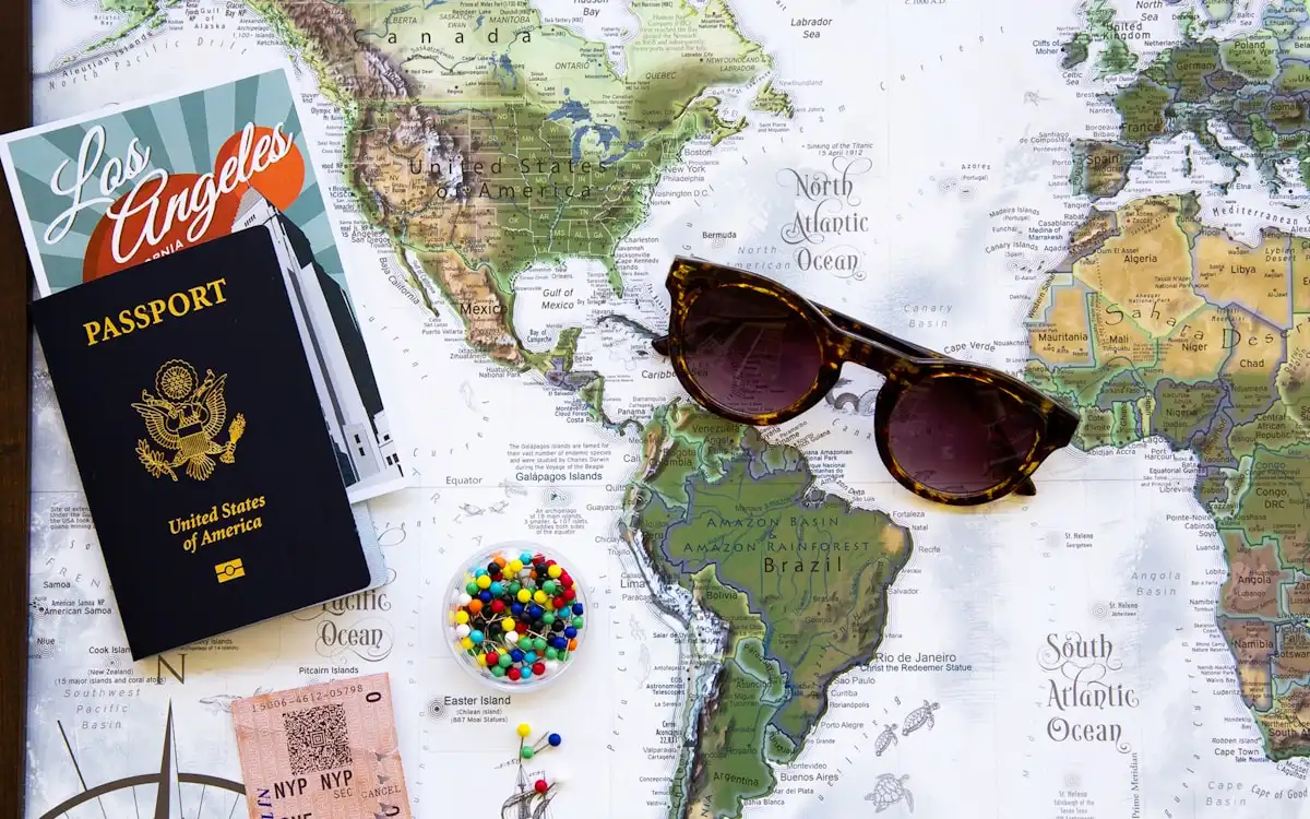 A world map with a passport, sunglasses and colorful map pins spread across it