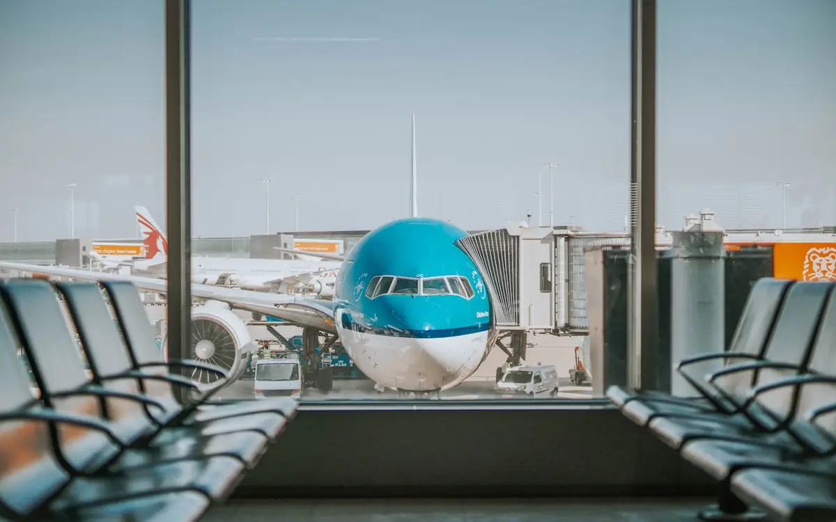 A blue and white passenger plane parked at a sunny airport gate, seen through the terminal window