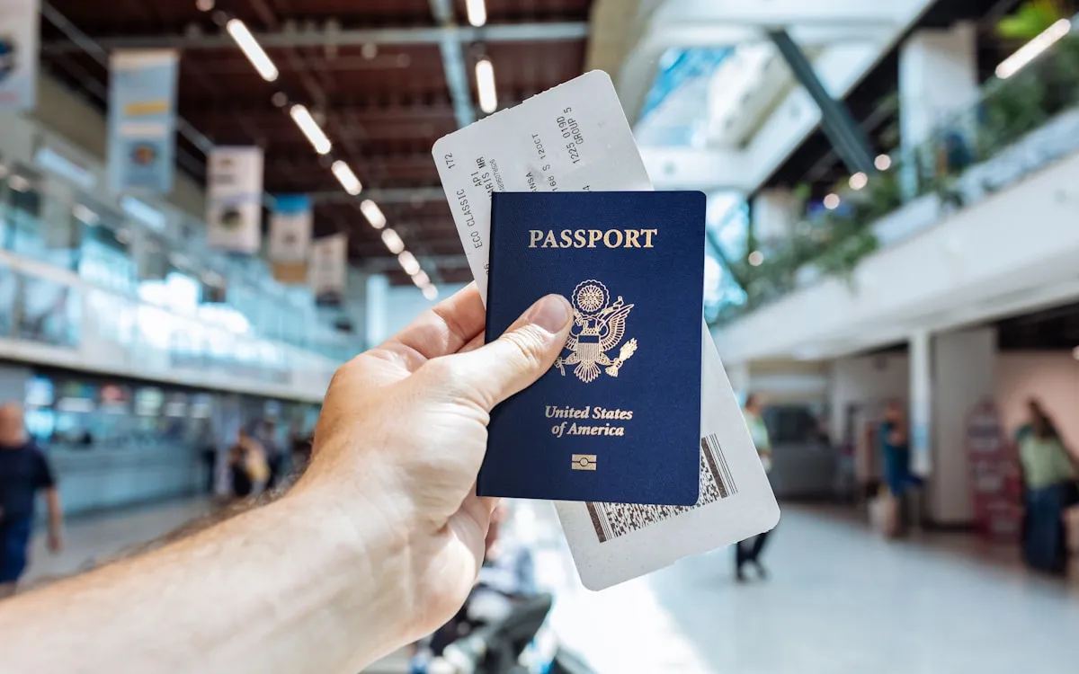 A hand holding a passport and a boarding pass together in a bright airport terminal